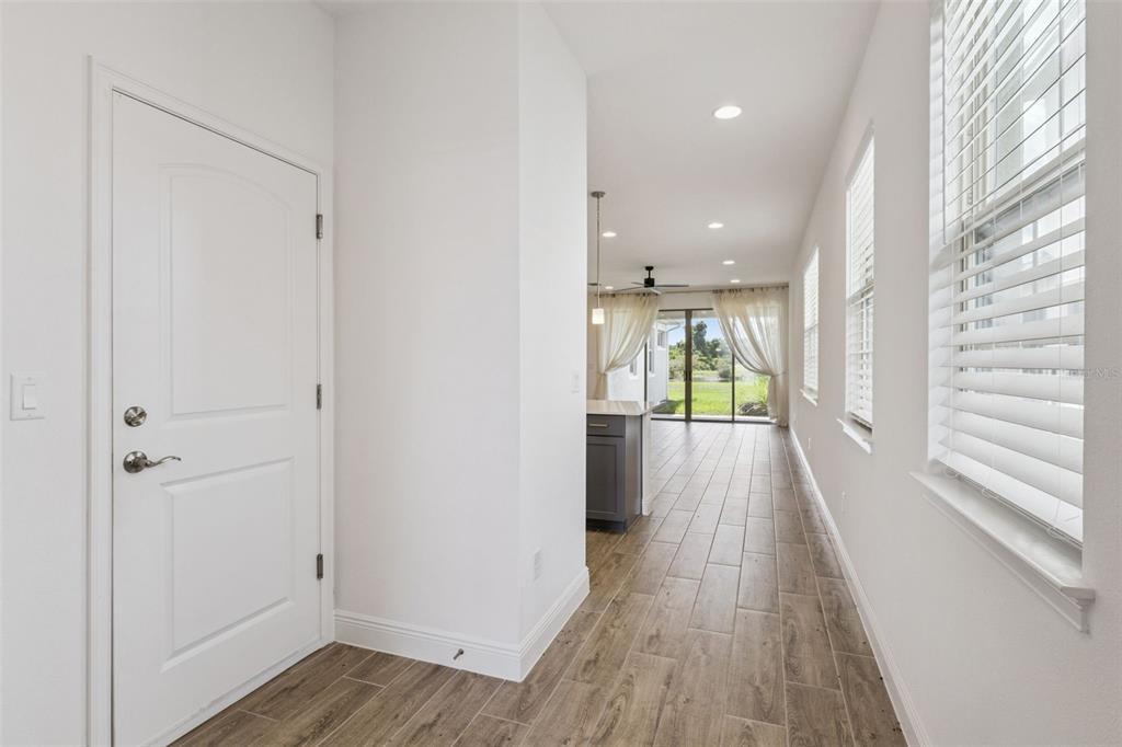A hallway with wood-look tile flooring leads to an open kitchen and living area — 3200 OXBOW COURT, HARMONY, FL