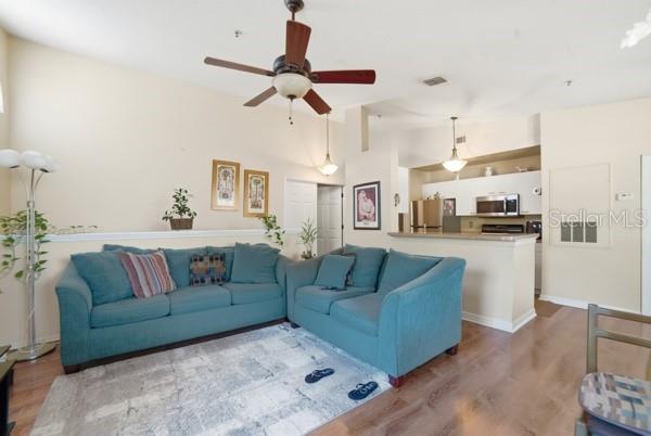A living room with a teal sectional sofa, a ceiling fan, and an open kitchen — 1601 COLUMBIA ARMS CIRCLE UNIT 201, KISSIMMEE, FL