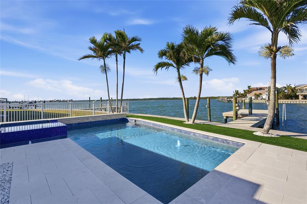 A swimming pool with a fountain overlooks a bay with a dock and palm trees — 16113 5TH STREET E, REDINGTON BEACH, FL