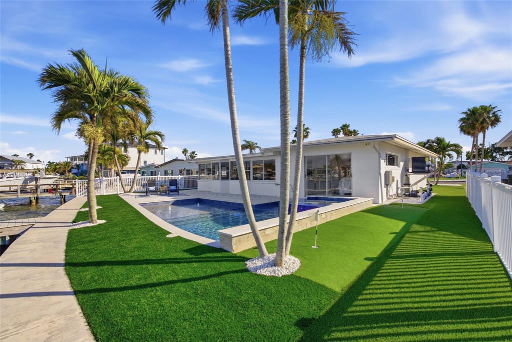 A backyard features a swimming pool, artificial turf, palm trees, and a white fence — 16113 5TH STREET E, REDINGTON BEACH, FL
