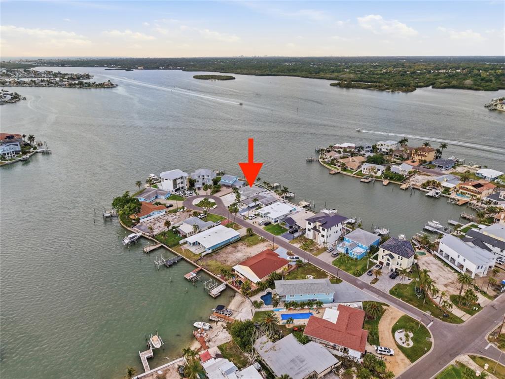 An aerial view shows a waterfront residential neighborhood with a red arrow pointing toward a house — 16113 5TH STREET E, REDINGTON BEACH, FL