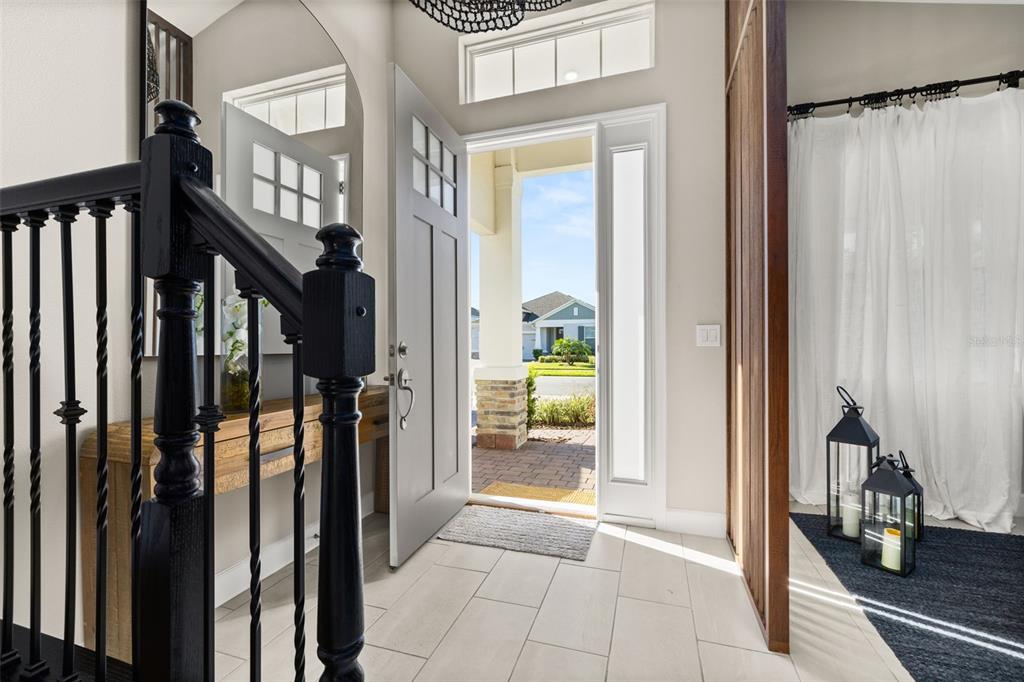 An entryway with a black staircase railing, light tile floors, and an open front door — 14321 WABASSO LOOP, WINTER GARDEN, FL
