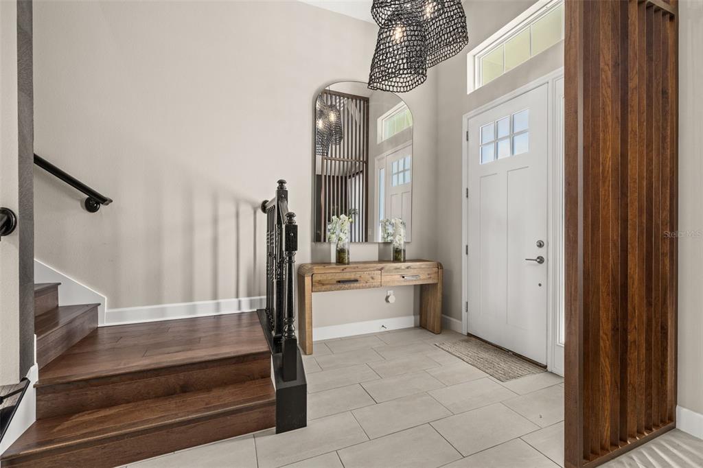 An entryway features a wooden console table, an arched mirror, a staircase, and a wood-slat partition — 14321 WABASSO LOOP, WINTER GARDEN, FL