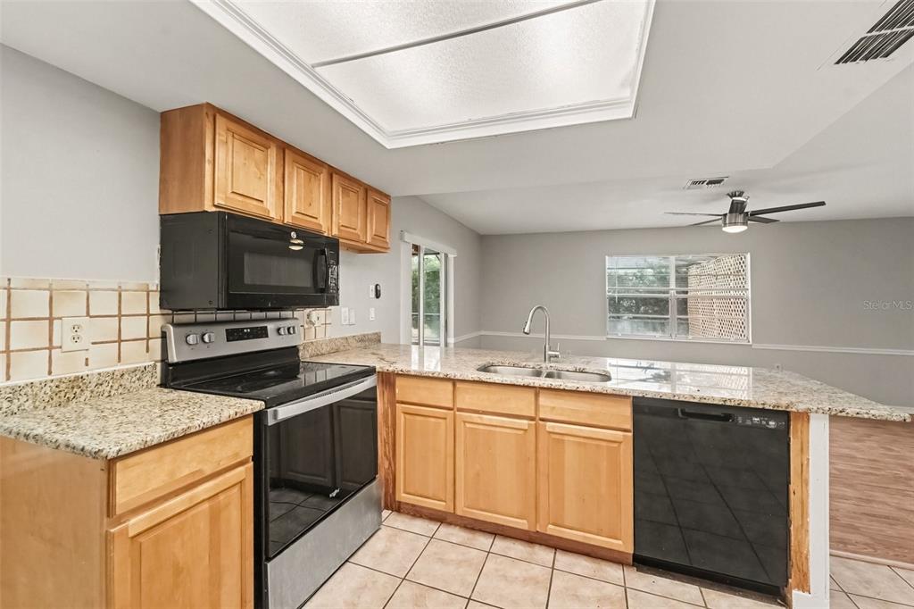 A kitchen features light wood cabinets, granite countertops, black appliances, and a tiled floor — 5296 FREEPORT DRIVE, SPRING HILL, FL