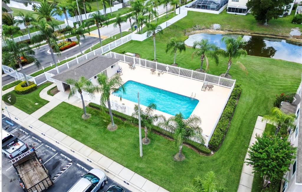 An aerial view shows a rectangular swimming pool enclosed by a white fence near a pond — 734 KENSINGTON LAKE CIR UNIT BRANDON, BRANDON, FL
