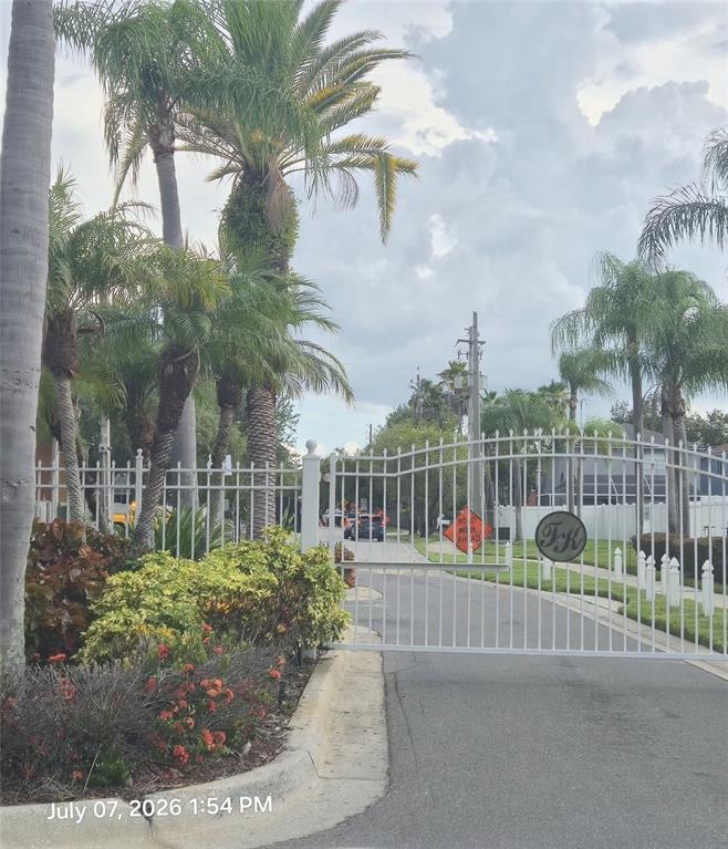 A white metal gate stands at the entrance of a residential community with palm trees — 734 KENSINGTON LAKE CIR UNIT BRANDON, BRANDON, FL