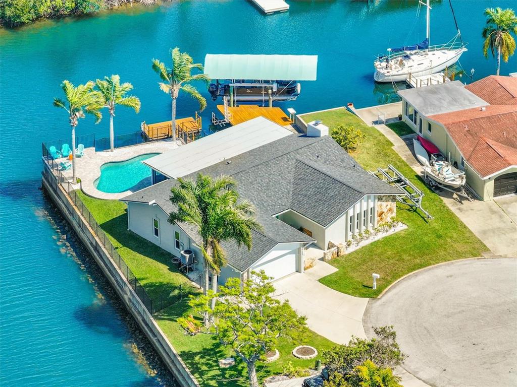 An aerial view shows a waterfront house with a pool, boat dock, and palm trees — 15722 DONZI DRIVE, HUDSON, FL