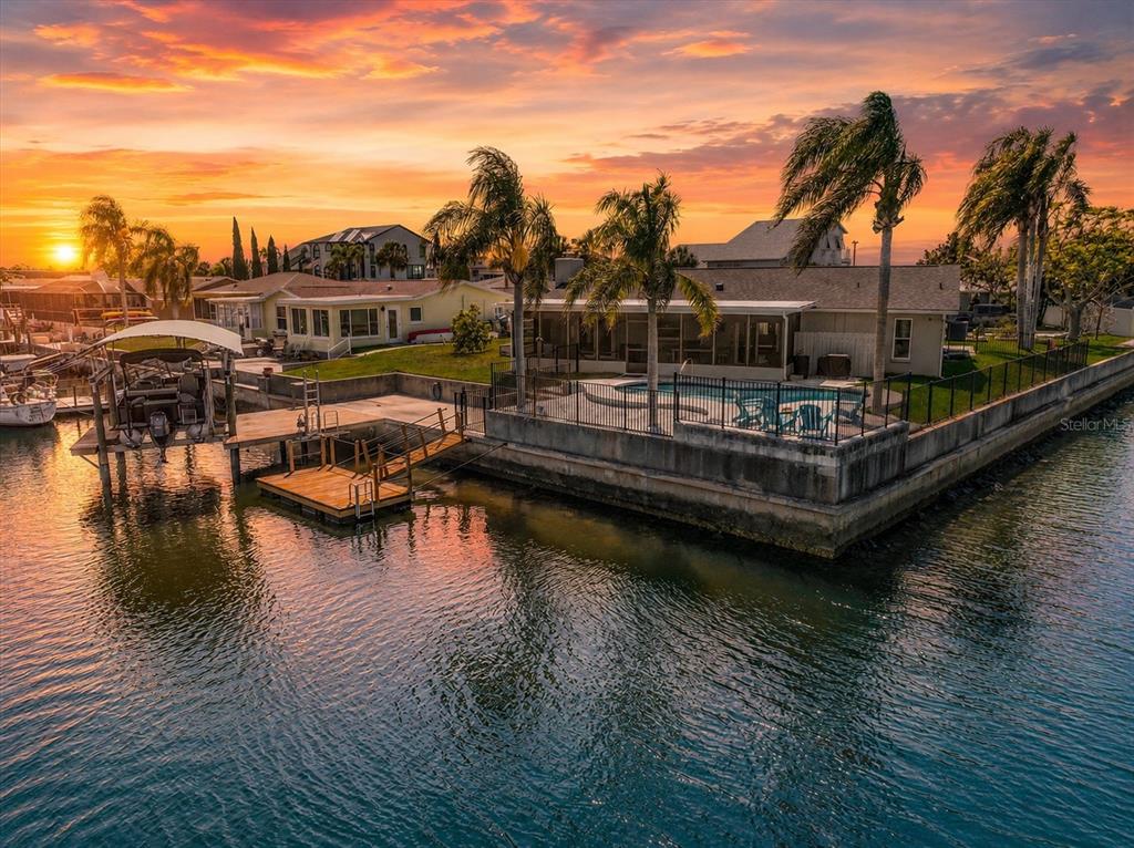 An aerial view of a waterfront house with a pool, dock, and boat lift at sunset — 15722 DONZI DRIVE, HUDSON, FL