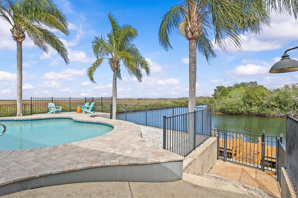 A swimming pool with a stone deck overlooks a canal and marshland under palm trees — 15722 DONZI DRIVE, HUDSON, FL