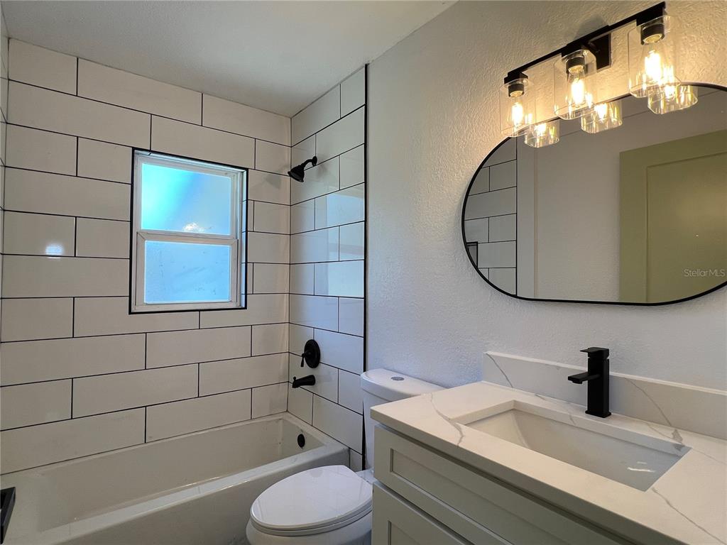 A bathroom features a white subway-tiled tub, a vanity with a marble top, and mirror — 2578 COVENTRY ROAD, MELBOURNE, FL