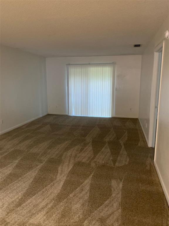An empty room with beige carpet, white walls, and a sliding glass door with blinds — 12125 NAPIERS CIRCLE, ORLANDO, FL
