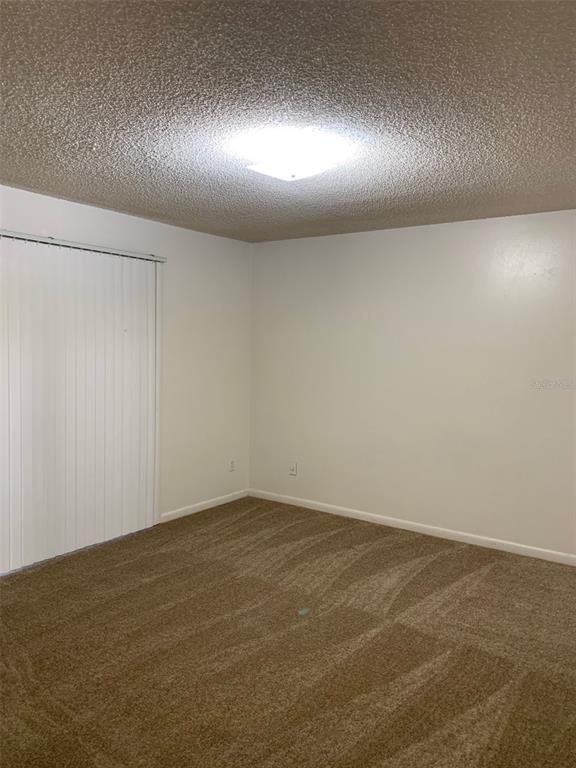 An empty room features beige carpet, white walls, a textured ceiling, and vertical window blinds — 12125 NAPIERS CIRCLE, ORLANDO, FL