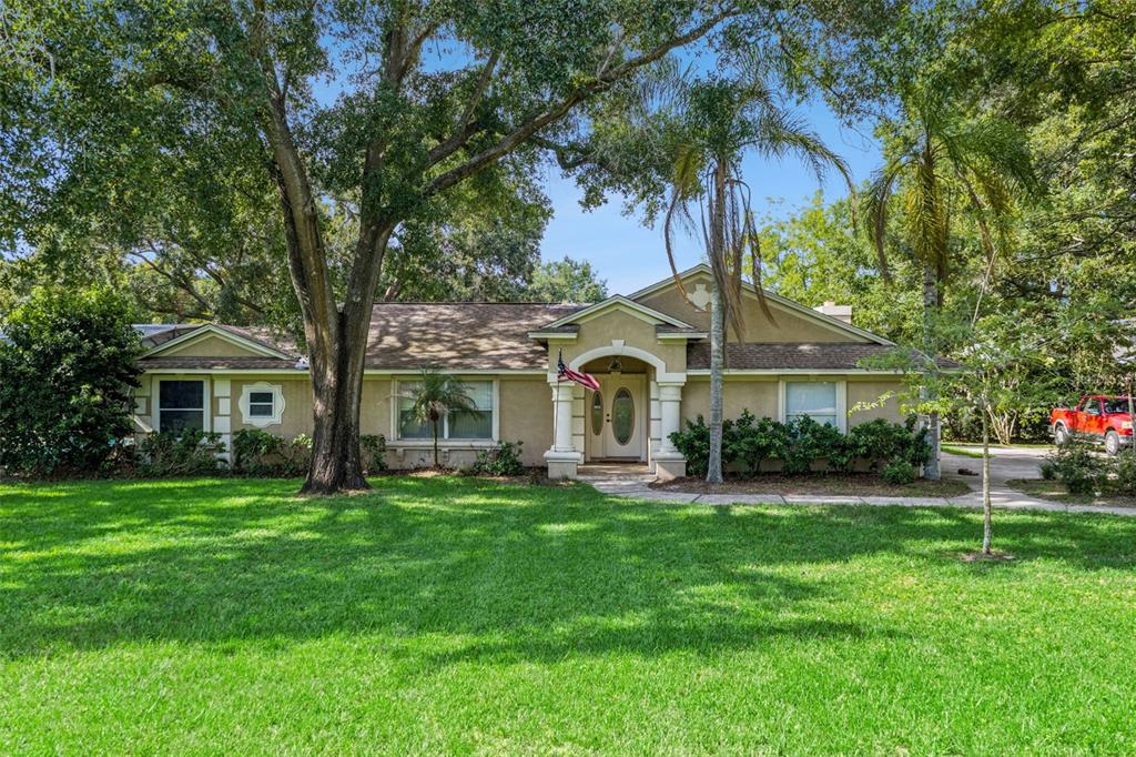 A single-story tan house with a front porch, large trees, and a green lawn — 10603 MOORE ROAD, GOTHA, FL