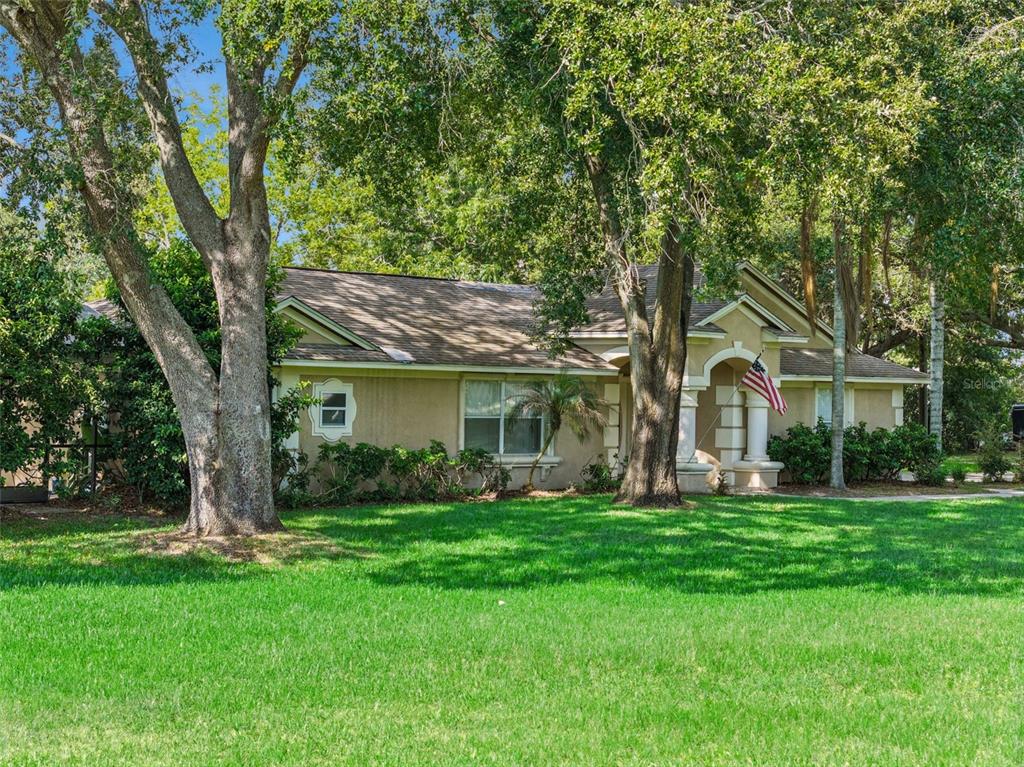 A single-story tan house with a shingled roof is surrounded by large trees and grass — 10603 MOORE ROAD, GOTHA, FL