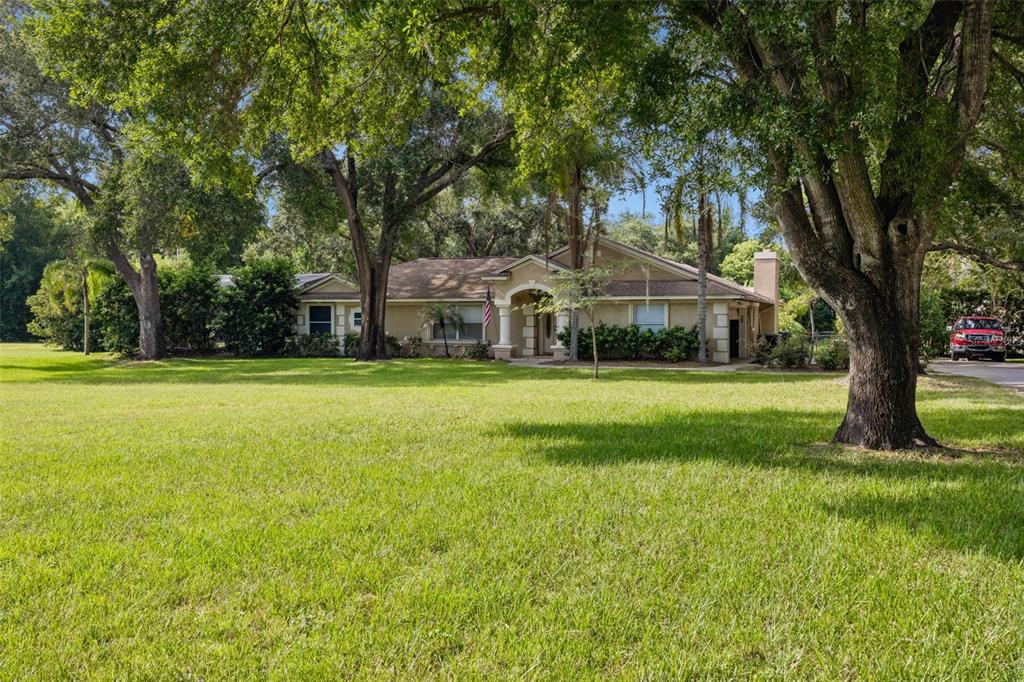 A single-story house with a large front lawn and mature trees under a blue sky — 10603 MOORE ROAD, GOTHA, FL