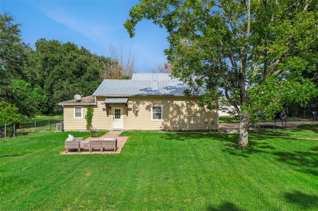 A one-story house with light-colored siding, a metal roof, and a small brick patio — 10603 MOORE ROAD, GOTHA, FL