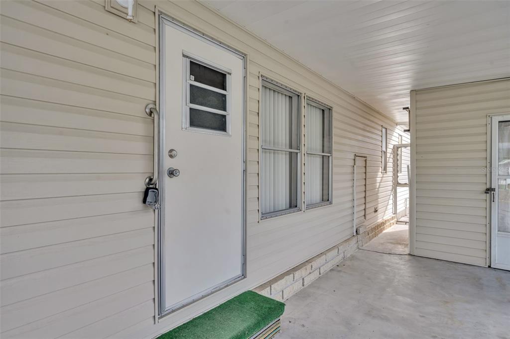 A white door with a lockbox and two windows on a beige vinyl-sided exterior wall — 53 KONO CIRCLE, LEESBURG, FL