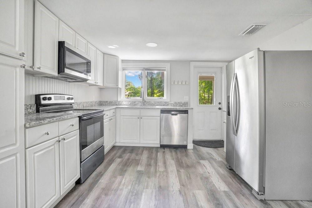A bright kitchen features white cabinets, stainless steel appliances, granite countertops, and wood-look flooring — 2012 E HARDING STREET, ORLANDO, FL