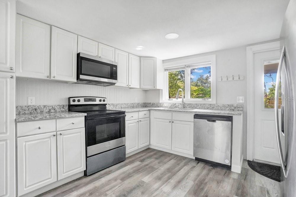 A kitchen with white cabinets, granite countertops, stainless steel appliances, and wood-look flooring — 2012 E HARDING STREET, ORLANDO, FL
