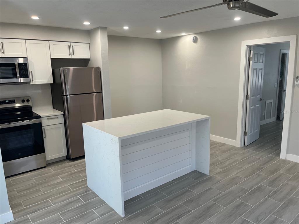 A kitchen features white cabinets, stainless steel appliances, a quartz island, and gray tile flooring — 1605 PASS A GRILLE WAY UNIT 1, ST PETE BEACH, FL