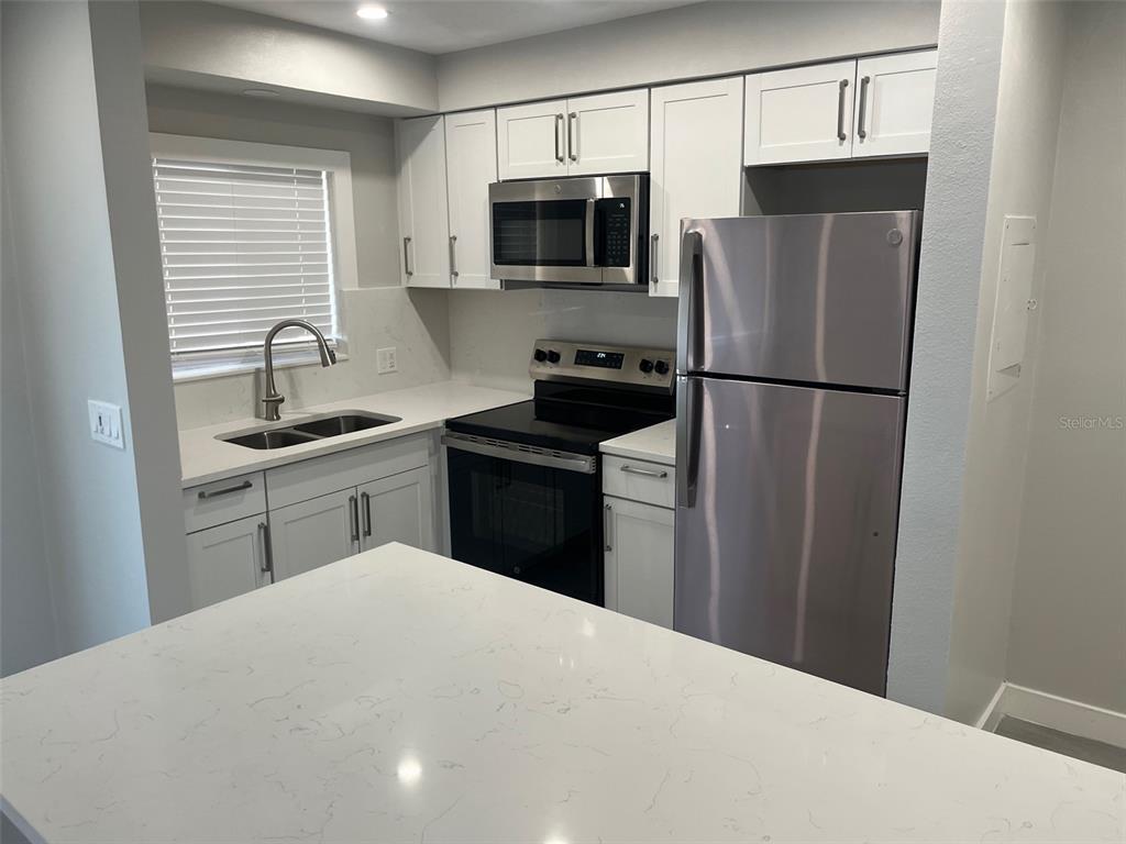A kitchen features white cabinets, stainless steel appliances, and a white quartz countertop island — 1605 PASS A GRILLE WAY UNIT 1, ST PETE BEACH, FL