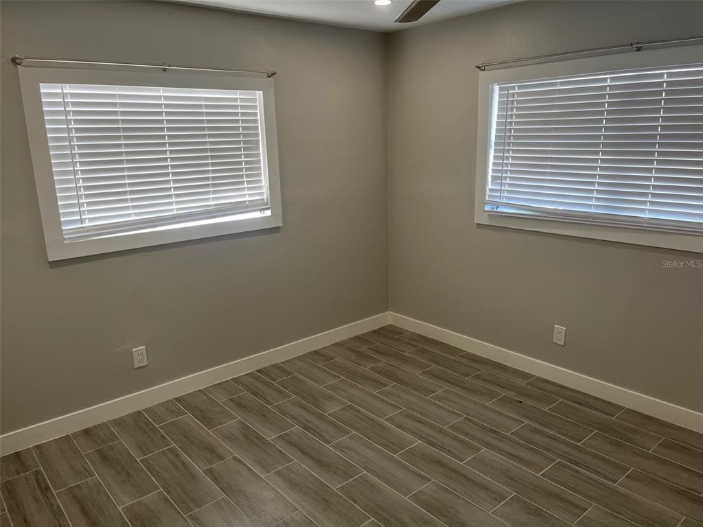 An empty room features gray walls, white trim, two windows with blinds, and wood-look tile flooring — 1605 PASS A GRILLE WAY UNIT 1, ST PETE BEACH, FL
