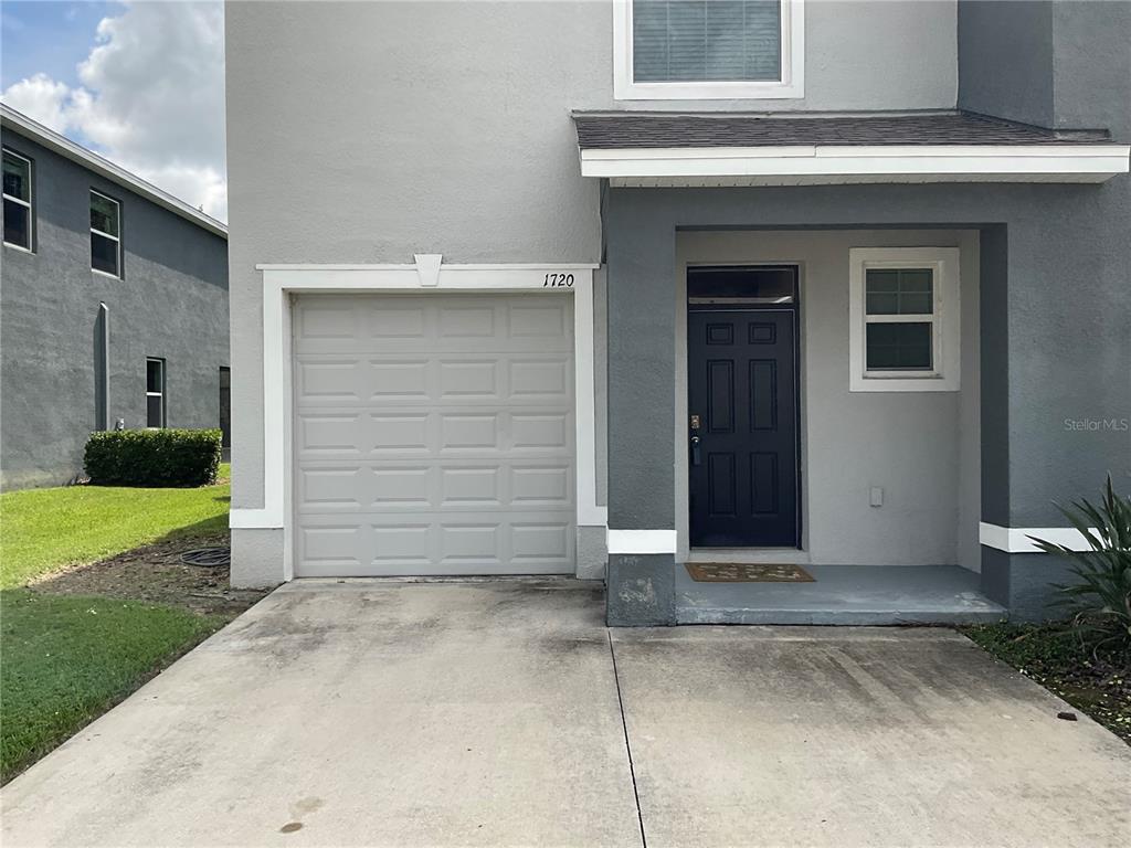 A two-story house exterior features a single-car garage, a dark blue front door, and stucco siding — 1720 HUBBELL ROAD, WESLEY CHAPEL, FL