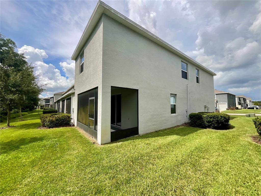 A two-story house exterior features a screened-in patio and a grassy side yard — 1720 HUBBELL ROAD, WESLEY CHAPEL, FL