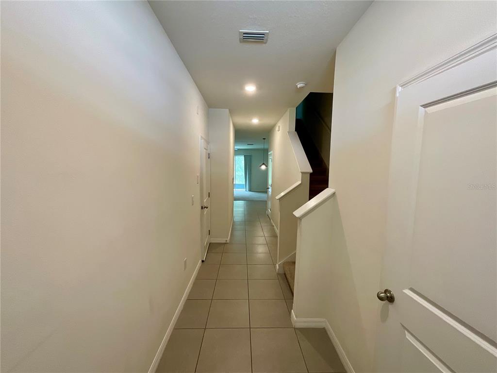 A hallway with tile flooring leads toward a staircase and a doorway at the end — 1720 HUBBELL ROAD, WESLEY CHAPEL, FL