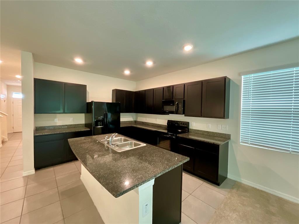 A kitchen features dark cabinetry, granite countertops, a central island, and tile flooring — 1720 HUBBELL ROAD, WESLEY CHAPEL, FL