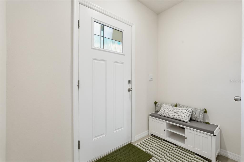 An entryway features a white front door, a storage bench with cushions, and striped flooring — 60 BELLA LAGO CIRCLE, PORT ORANGE, FL