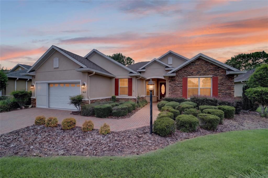 A single-story house with a stone facade, red shutters, and a brick walkway at sunset — 8815 SW 83RD COURT ROAD, OCALA, FL