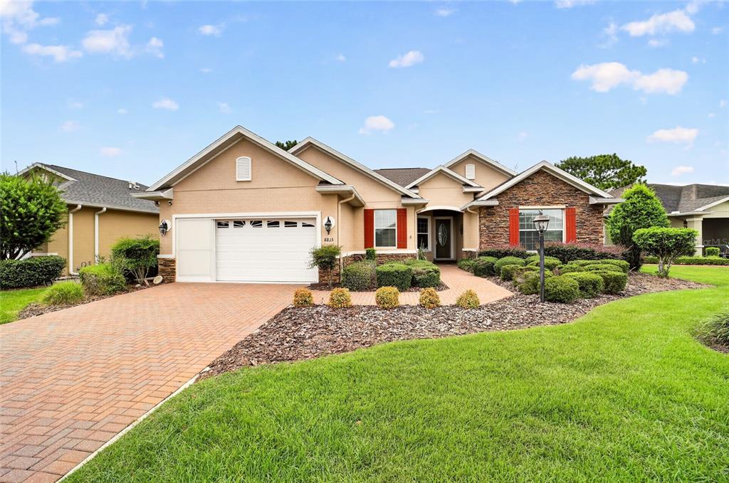 A single-story house with a brick driveway, stone facade, and manicured landscaping under a blue sky — 8815 SW 83RD COURT ROAD, OCALA, FL