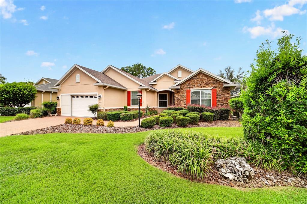 A single-story house with a tan exterior, stone accents, red shutters, and a green lawn — 8815 SW 83RD COURT ROAD, OCALA, FL