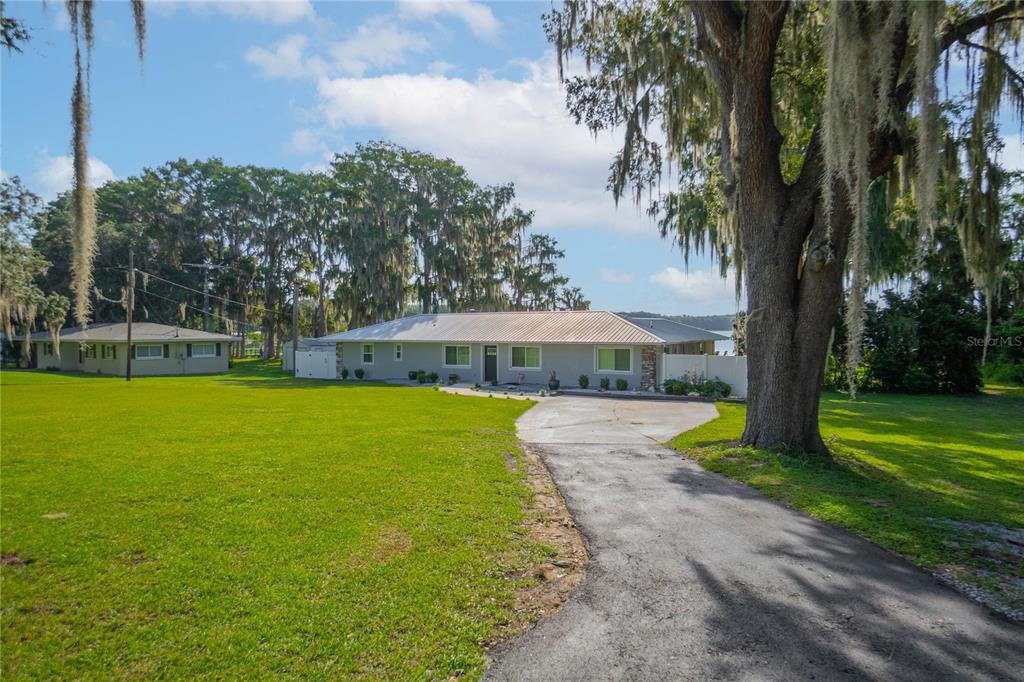 A single-story house with a metal roof sits on a large lawn with mature trees — 221 S HUNTING LODGE DRIVE, INVERNESS, FL