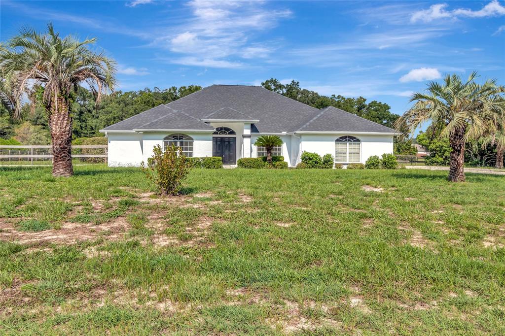A white single-story house with a dark roof stands behind a grassy yard with palm trees — 6856 NE 61ST AVENUE ROAD, SILVER SPRINGS, FL