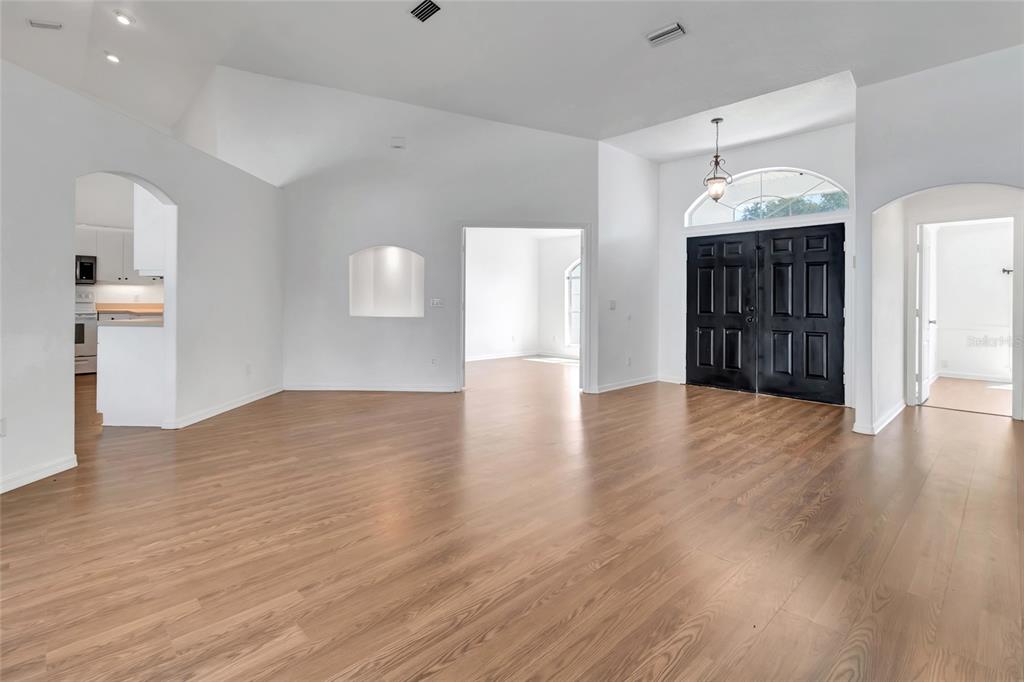 An open living area features light wood floors, white walls, and a black double door — 6856 NE 61ST AVENUE ROAD, SILVER SPRINGS, FL