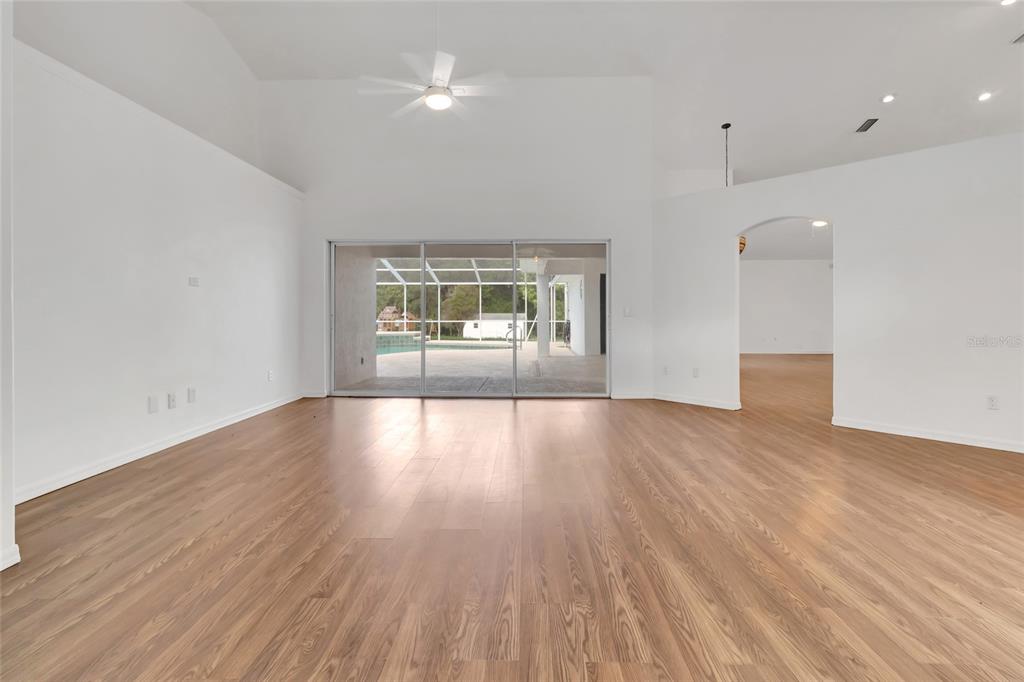 A spacious living room with high ceilings, wood-look flooring, and sliding glass doors to a pool — 6856 NE 61ST AVENUE ROAD, SILVER SPRINGS, FL
