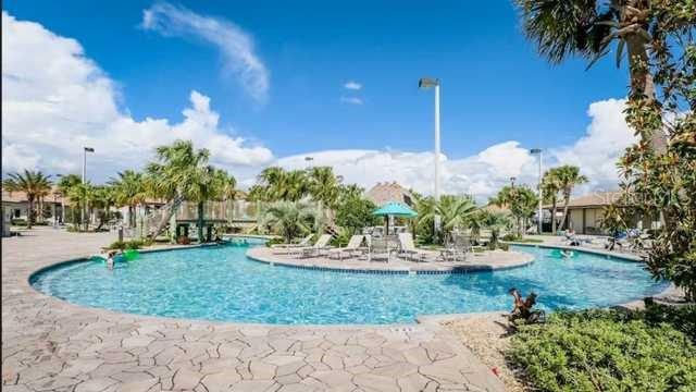 A resort-style swimming pool with lounge chairs and palm trees under a bright blue sky — 4352 ACORN COURT, DAVENPORT, FL