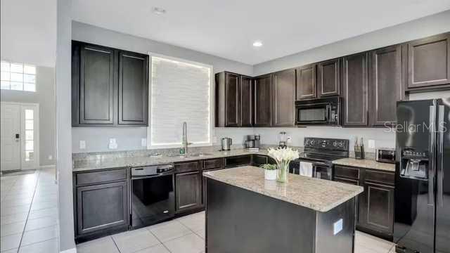 A kitchen features dark wood cabinets, granite countertops, a center island, and black appliances — 4352 ACORN COURT, DAVENPORT, FL