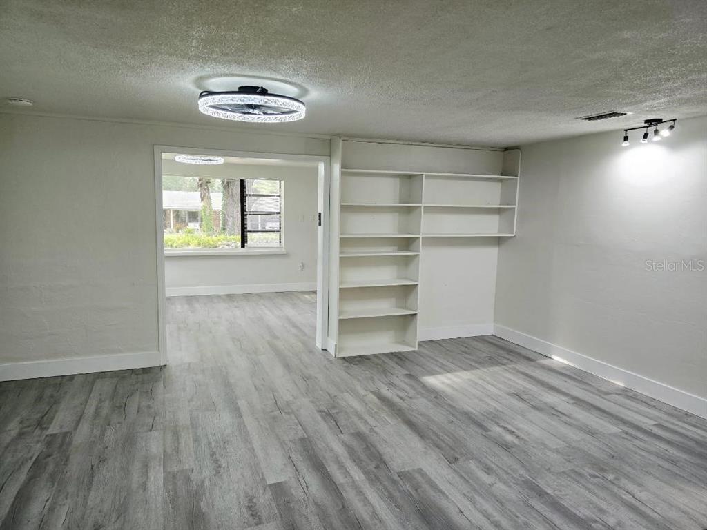 A room with gray wood-look flooring, a built-in white bookshelf, and a doorway to another room — 234 E LADY LAKE BOULEVARD, LADY LAKE, FL