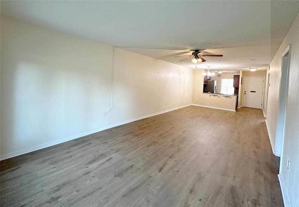 A spacious living room with light wood-look flooring, a ceiling fan, and an open kitchen — 1279 MISSION HILLS BOULEVARD, CLEARWATER, FL