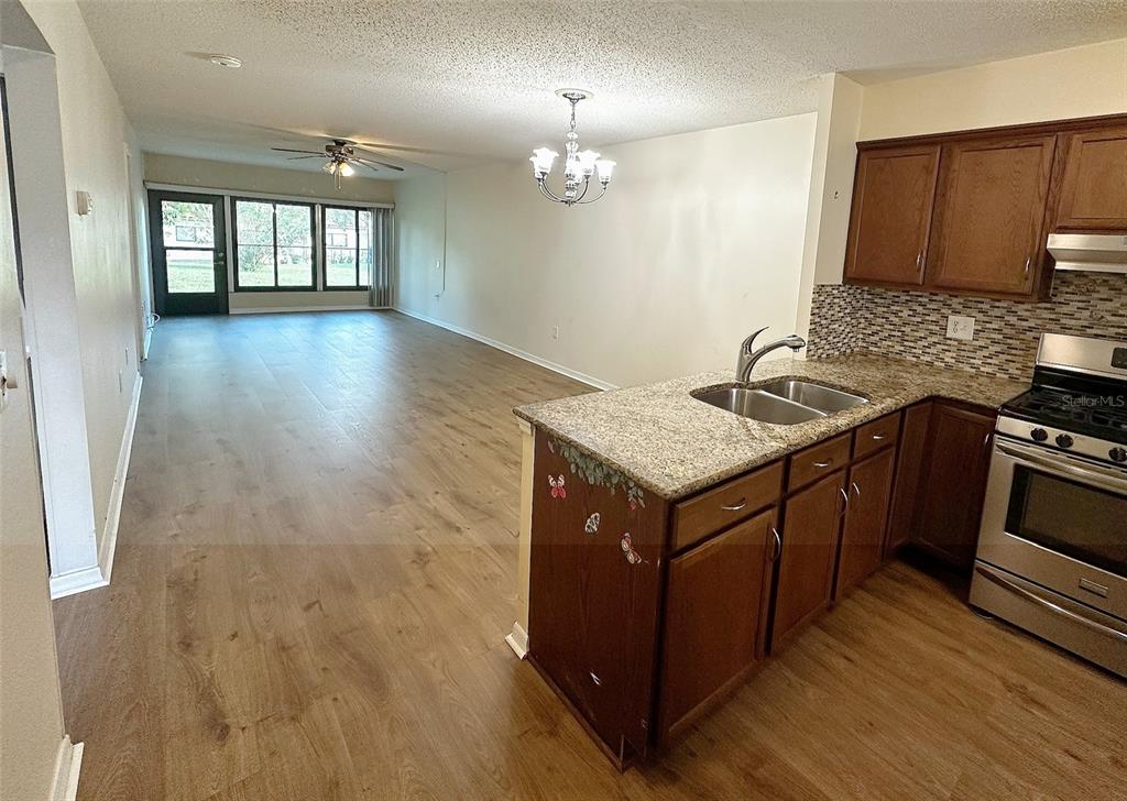 An open-concept kitchen with granite countertops overlooks a living area with wood-look flooring — 1279 MISSION HILLS BOULEVARD, CLEARWATER, FL