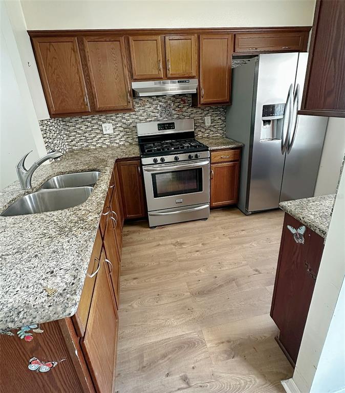 A kitchen features wood cabinets, granite countertops, stainless steel appliances, and light wood-look flooring — 1279 MISSION HILLS BOULEVARD, CLEARWATER, FL