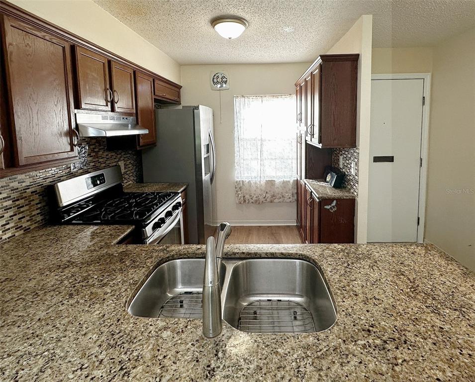 A kitchen features dark wood cabinets, granite countertops, stainless steel appliances, and a double sink — 1279 MISSION HILLS BOULEVARD, CLEARWATER, FL