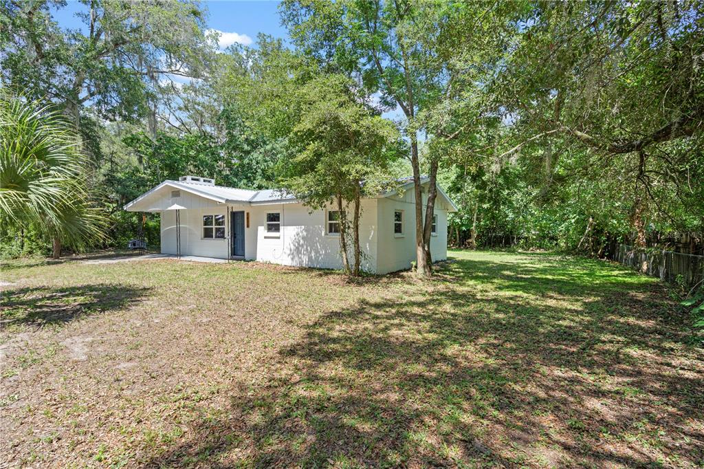A white, single-story house with a metal roof sits on a grassy, tree-shaded lot — 1825 SE 47TH TERRACE, GAINESVILLE, FL