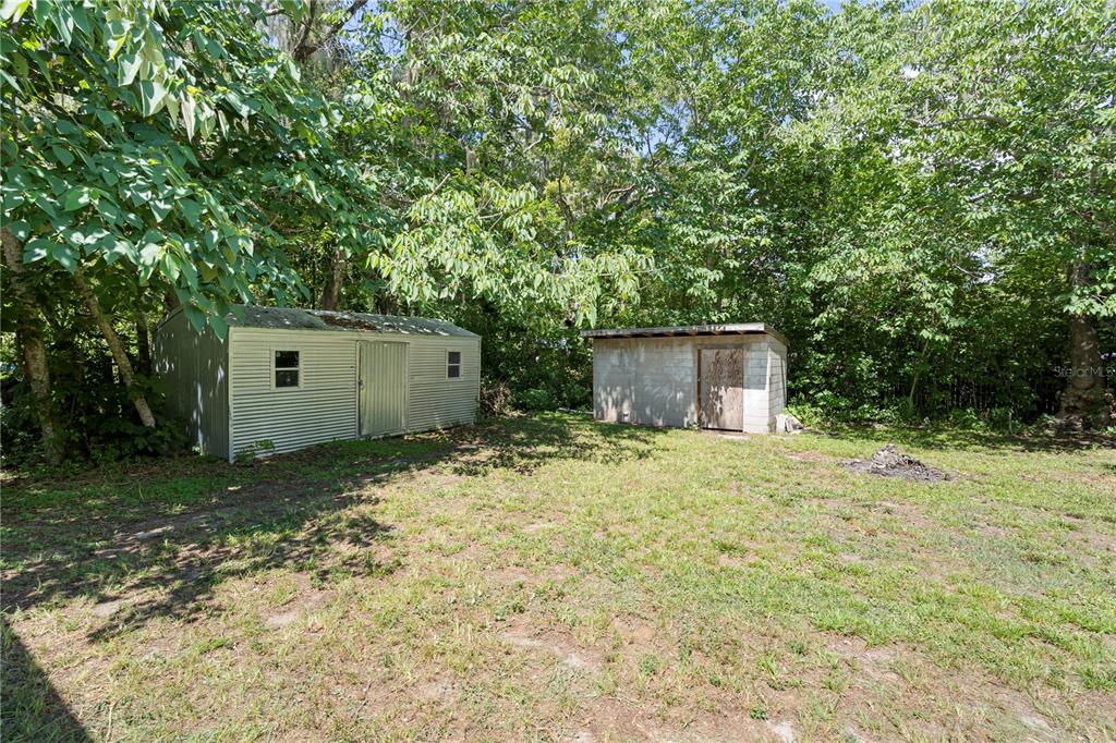 Two storage sheds sit on a grassy lot surrounded by dense trees — 1825 SE 47TH TERRACE, GAINESVILLE, FL