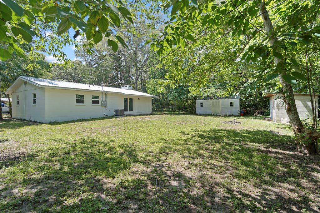 A white house with a metal roof stands next to two sheds in a backyard — 1825 SE 47TH TERRACE, GAINESVILLE, FL