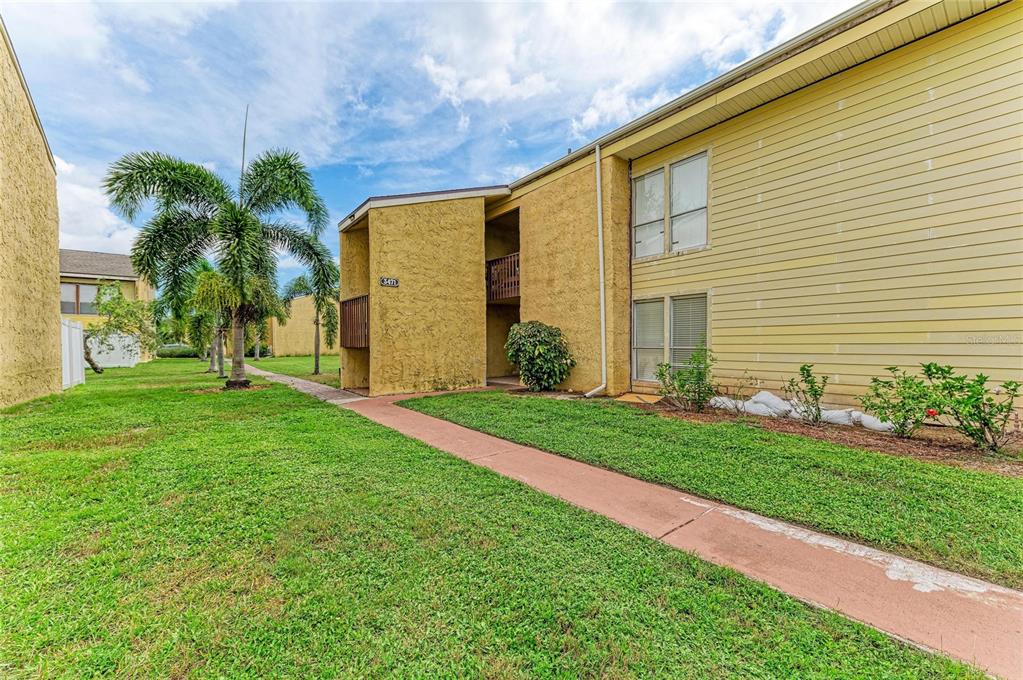 A yellow two-story apartment building with a sidewalk and palm trees on a grassy lawn — 3471 CLARK ROAD UNIT 169, SARASOTA, FL