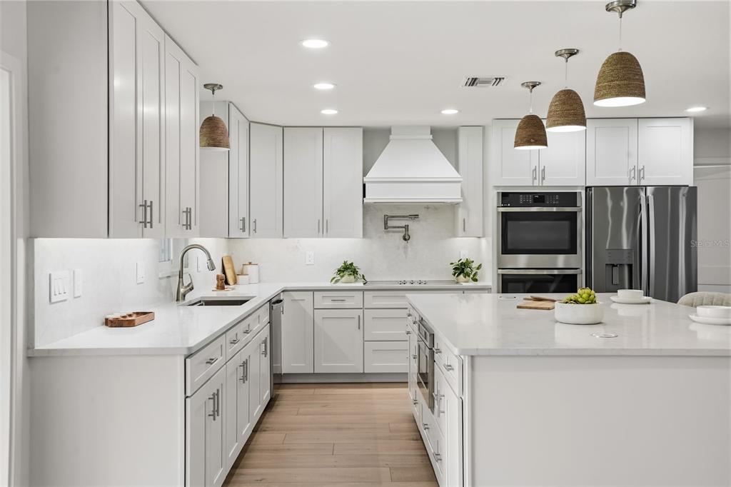 A modern kitchen features white cabinetry, quartz countertops, stainless steel appliances, and a large island — 39251 COUNTY ROAD 439, UMATILLA, FL